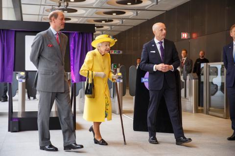 女王陛下身穿黄色外套，头戴帽子，与伦敦交通局局长安迪·拜福德和爱德华王子在一起, the Earl of Wessex on her left